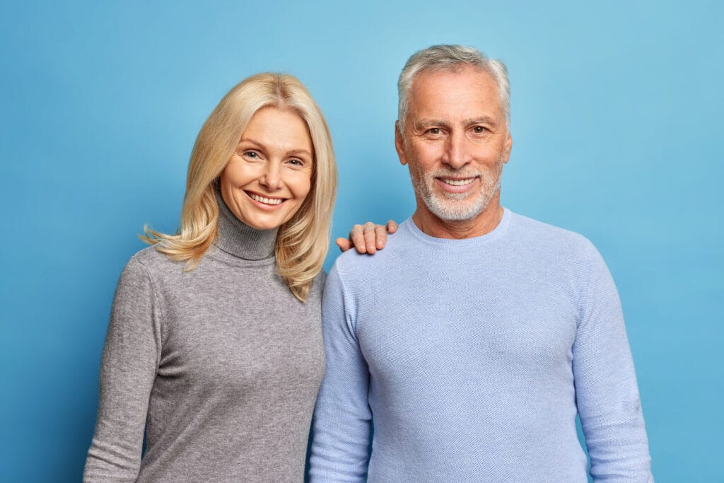 Photo of happy senior woman and man express positive emotions pose together being still in love isolated over blue background. Smiling grandmother grandfather make family photo glad to meet children